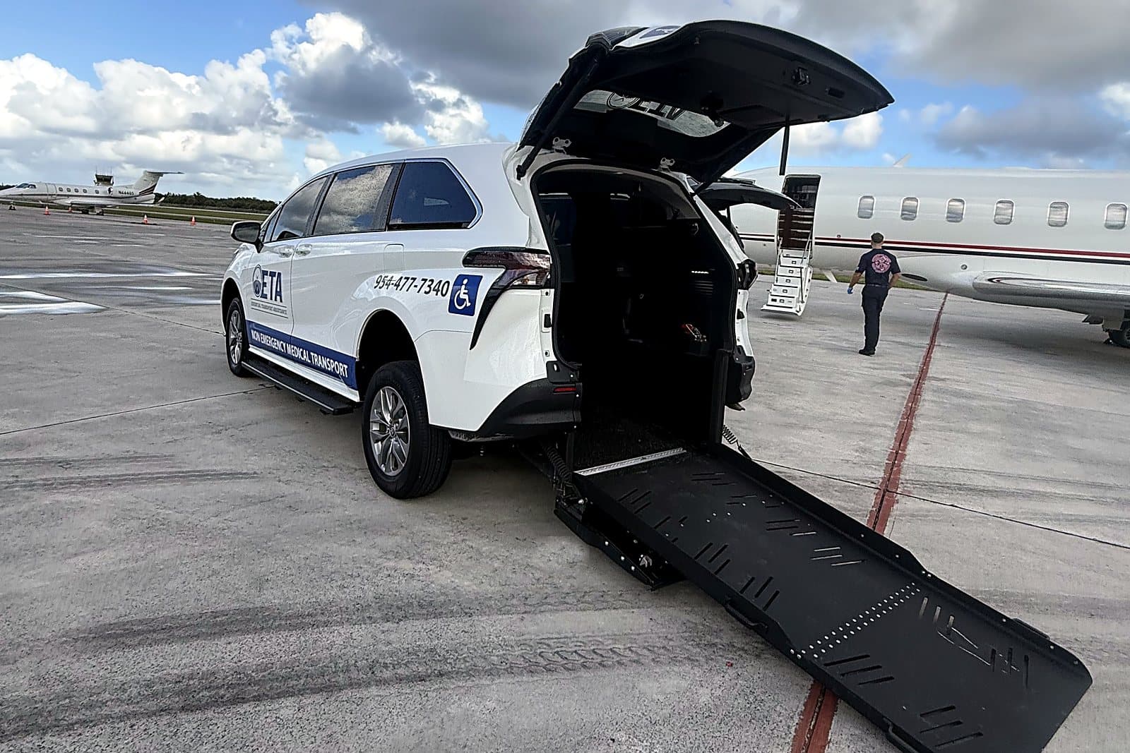 ETA wheelchair-accessible minivan with its rear ramp lowered beside a private jet at Boca Raton Airport