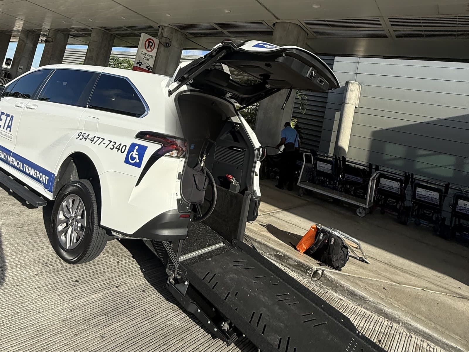 Essential Transport Assistance wheelchair-accessible minivan with its rear ramp lowered at the Fort Lauderdale-Hollywood International Airport terminal curb