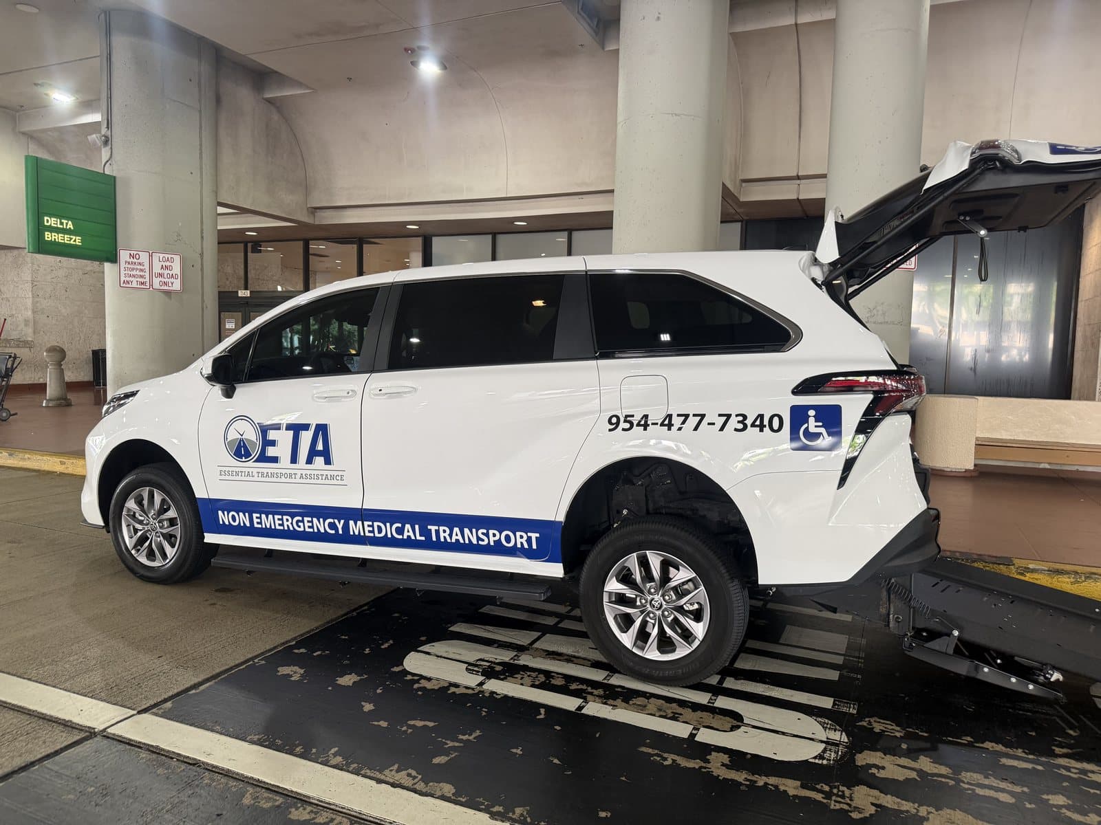Essential Transport Assistance wheelchair-accessible minivan at the Palm Beach International Airport terminal curb with its rear ramp lowered